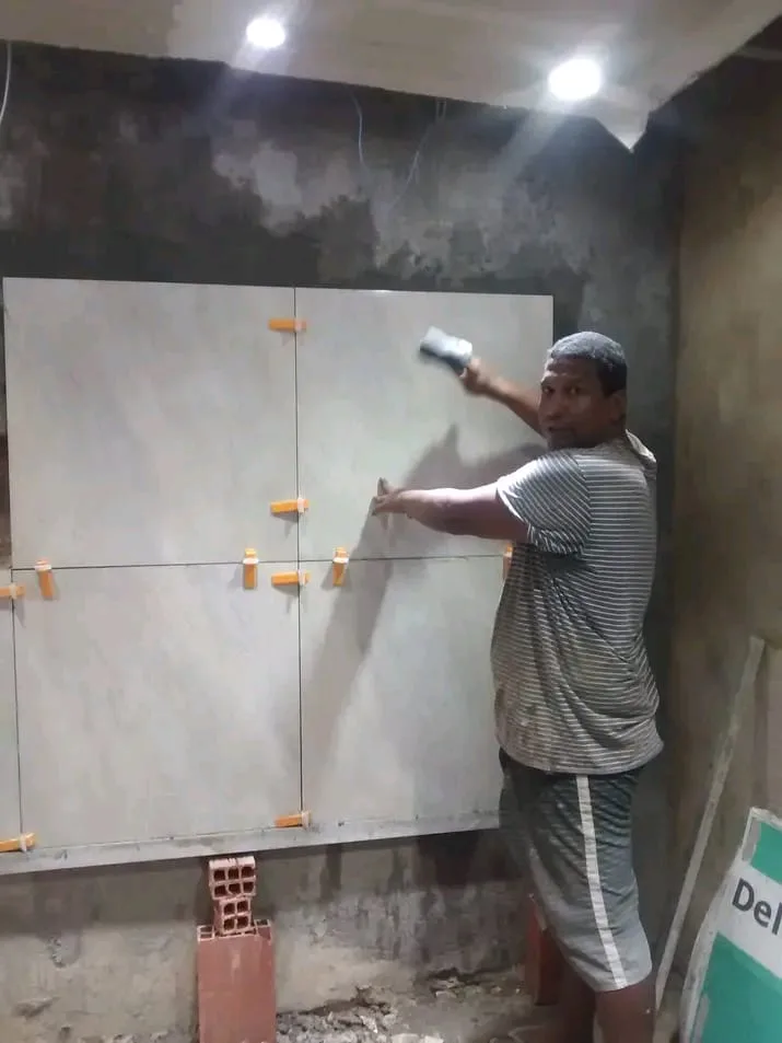 Pedreiro assentando porcelanato grande na parede, com niveladores